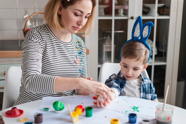 Beautiful mother teaching little boy how to paint eggs