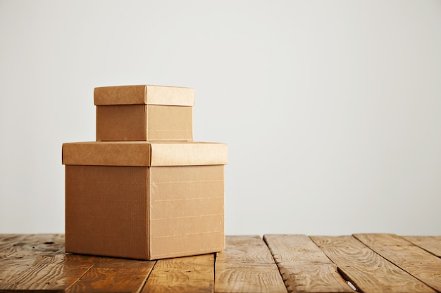 Free photo beautiful old uneven wooden table with two blank similar cardboard boxes with covers against white wall background