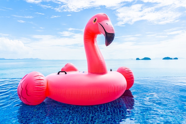 Beautiful outdoor swimming pool in hotel resort with flamingo float around sea ocean white cloud on blue sky