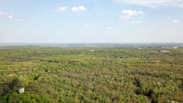 Beautiful panoramic view of a green spring forest and city in the distance against a blue sky background Photo from the drone