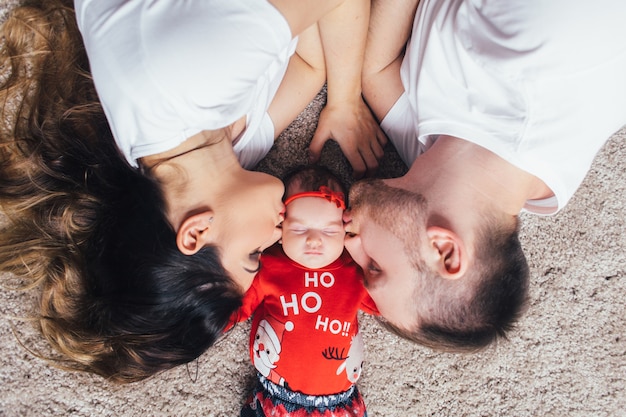 The beautiful parents kissing their daughter and liing on the floor