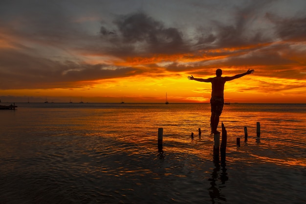 Free photo beautiful picture of a male silhouette standing on the wooden stilts on the water