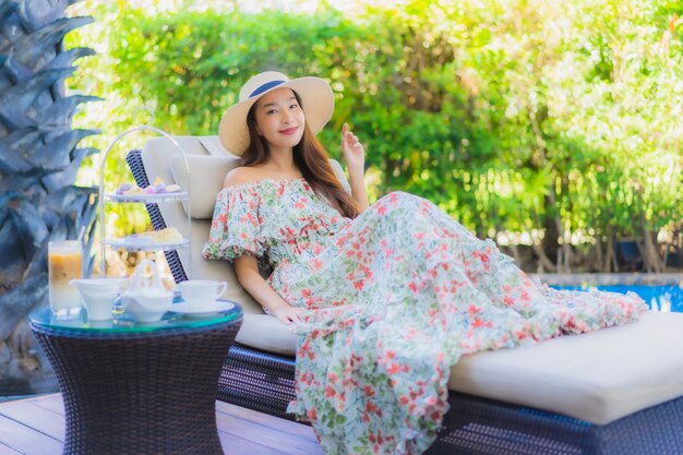 Beautiful portrait young asian woman with afternnoon tea set with coffee sit on chair around swimming pool