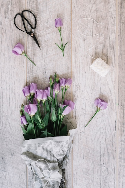 Beautiful purple eustoma flowers bouquet with scissor and white spool on wooden background