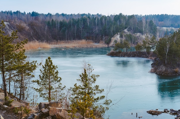 Beautiful quarry near lake covered with thin ice