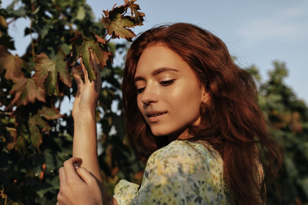 Free Photo beautiful red haired girl with freckles in yellow and green cool outfit looking down and posing on vineyards