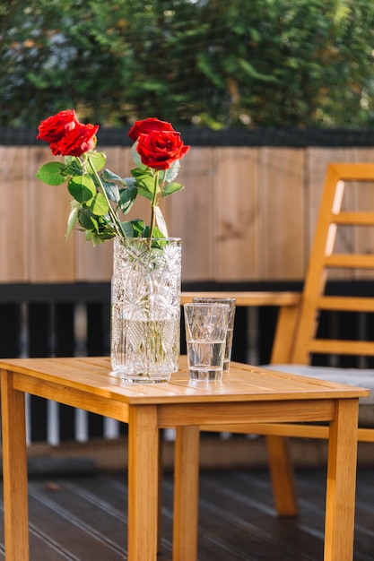 Free photo beautiful red rose in vase and drink glasses on wooden table