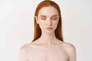 Free photo beautiful redhead woman with pale skin and freckles standing without makeup clean smooth face closed eyes and calm expression standing over white background