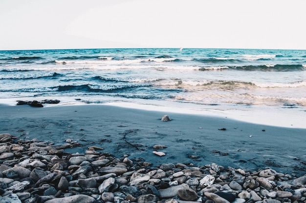 Beautiful rocky and sandy beach of the sea with medium waves under a clear blue sky