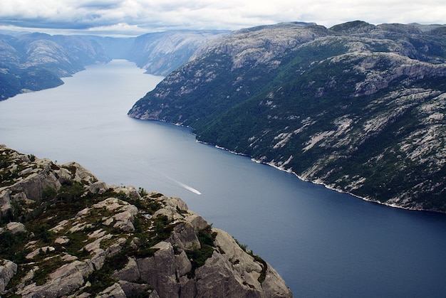 Beautiful scenery of famous Preikestolen cliffs near a lake under a cloudy sky in Stavanger