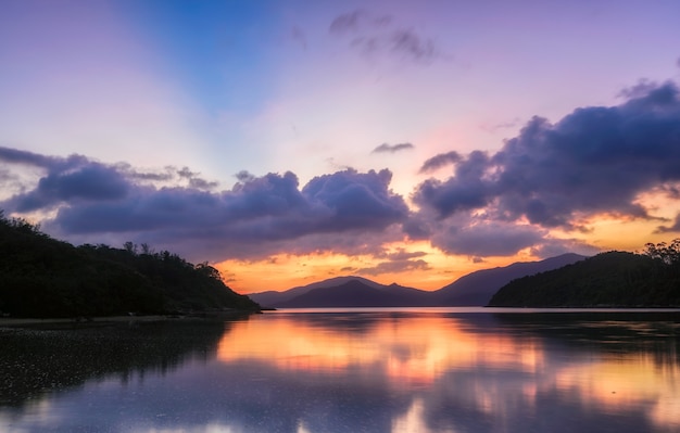 Beautiful scenery of a lake surrounded by forested mountains under a purple sky at sunset