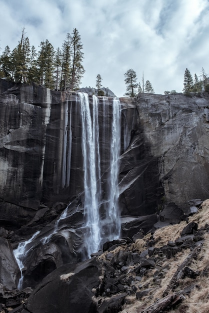 Free photo beautiful scenery of a powerful waterfall flowing through a rocky cliff under a cloudy sky