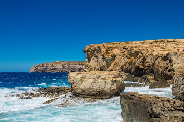 Beautiful scenery of a rocky cliff near the sea waves under the beautiful blue sky