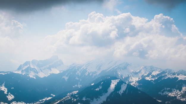 Beautiful scenery of white fluffy clouds covering high mountains during daytime