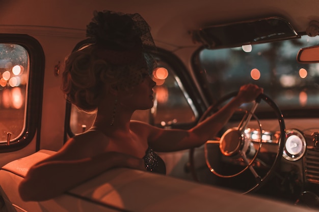 beautiful sexy fashion blond girl model with bright makeup and curly hairstyle in retro style sitting in old car