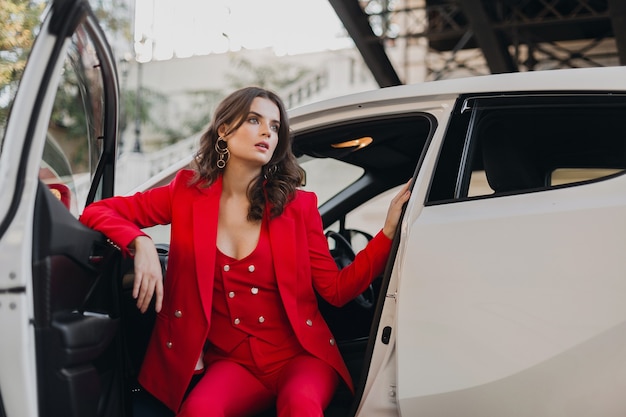 Beautiful sexy rich business woman in red suit posing in white car