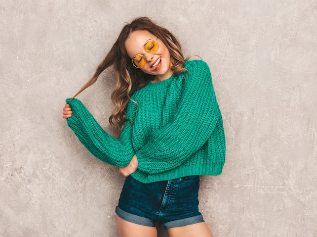 Free Photo beautiful sexy smiling gorgeous girl in green trendy sweater. woman posing in round sunglasses. model having fun and showing her tongue