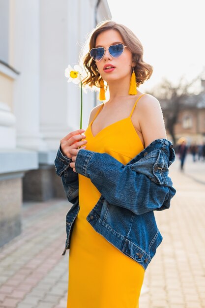 Beautiful sexy stylish woman in yellow stylish dress wearing denim jacket, trendy outfit, spring summer fashion trend, sunny, blue sunglasses, street fashion, hipster style, fashionable accessories