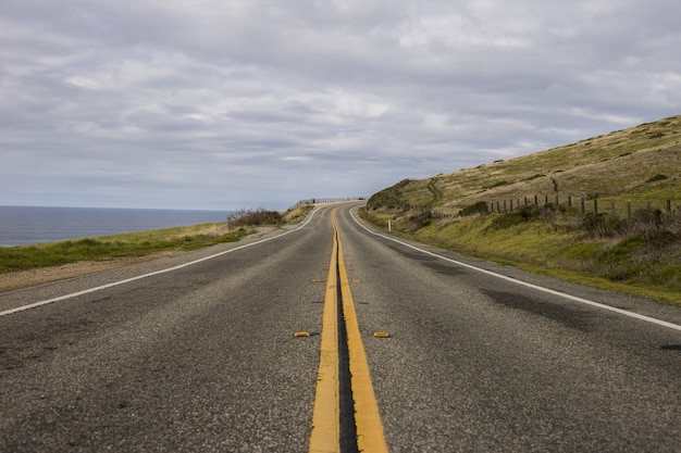 Beautiful shot of an asphalt road surrounded by mountains and the ocean on a cloudy day