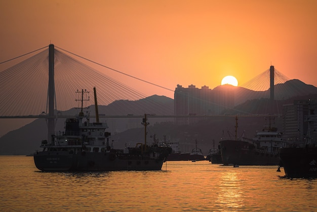 Beautiful shot of boats sailing in the sea with a bridge on the background at sunset