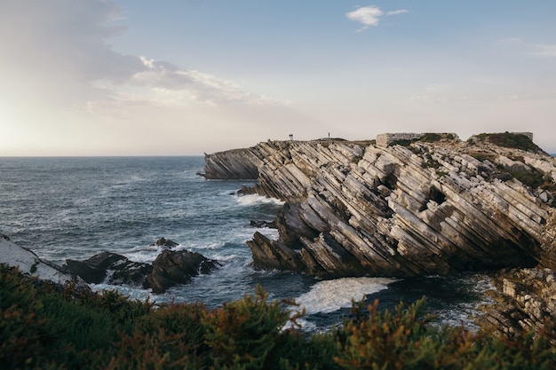 Free photo beautiful shot of a bush-covered coastline with tilted sandstone rock formations in peniche