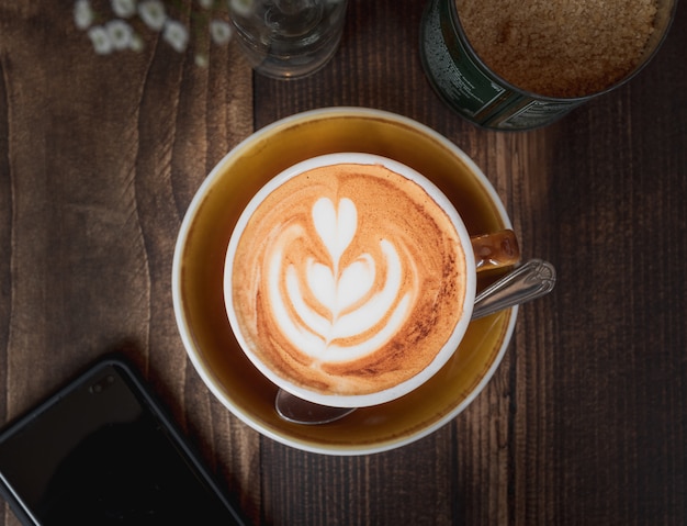 Free photo beautiful shot of a cup of cappuccino with a white heart pattern on a wooden table