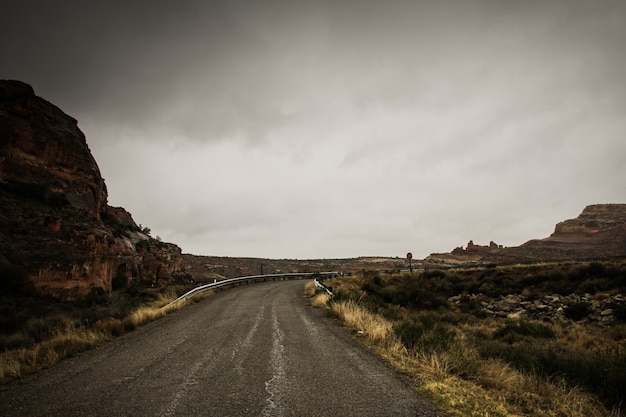 Free Photo beautiful shot of an empty road in the middle of rocks and dry grass field under a cloudy sky