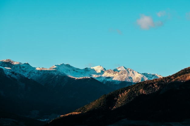 Beautiful shot of forested hills and snowy mountain in the distance with blue sky