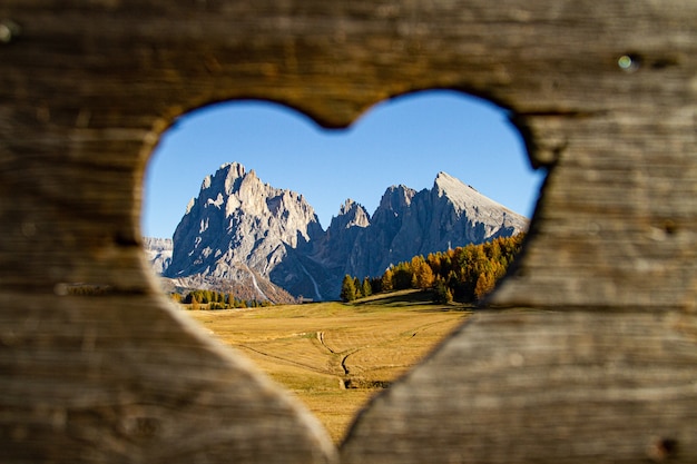 Free photo beautiful shot from heart shaped whole of mountains and green trees in distance in dolomite italy