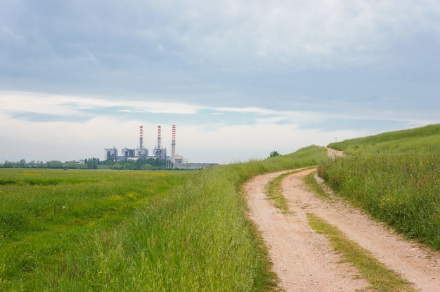 Beautiful shot of a green field at the side of a dirt road with a building and a cloudy sky