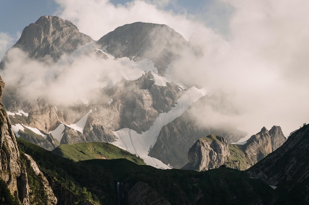 Free photo beautiful shot of green mountains covered with white clouds in a clear blue sky