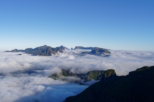 Free Photo beautiful shot of green mountains and hills covered in white clouds in a clear sky