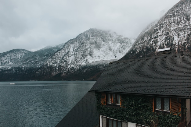 Free photo beautiful shot of a house near the lake and gray mountains covered with snow during the daytime