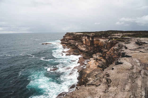 Free Photo beautiful shot of a large cliff next to blue water on a gloomy day