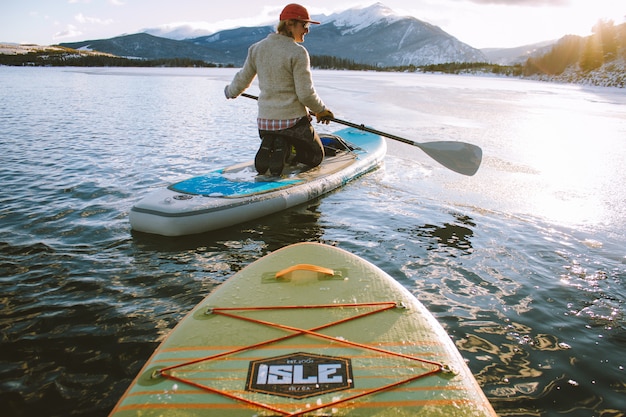 Free photo beautiful shot of a male sitting on a paddleboard holding an oar with mountains