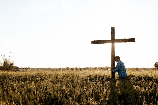 Beautiful shot of a male with his head against the wooden cross in a grassy field