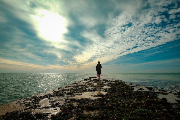 Beautiful shot of a person walking on a land inside the ocean under the cloudy sky