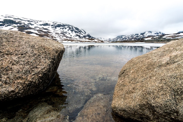 Free photo beautiful shot of rocks by the river and snowy mountain in norway