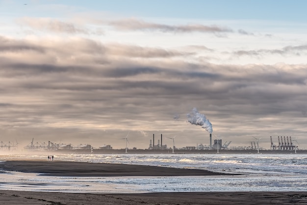 Free photo beautiful shot of a sea with windmills and factory in the distance under a cloudy sky