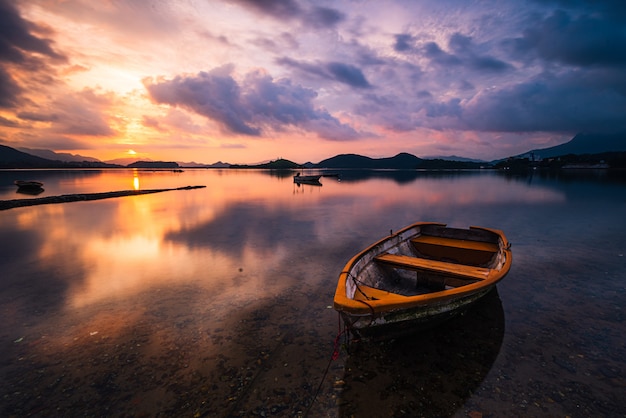 Beautiful shot of a small lake with a wooden rowboat in focus and amazing clouds in the sky