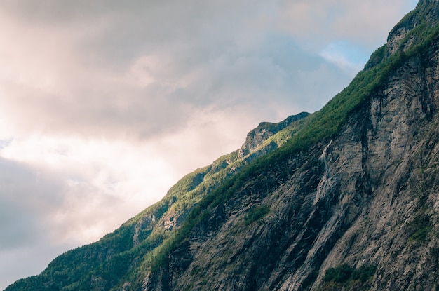 Free photo beautiful shot of a steep cliff with greenery on it in the mountains on a cloudy day