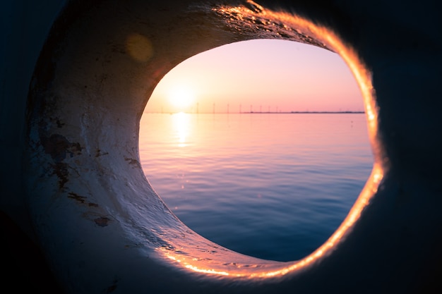 Beautiful shot of the view of a sunset at sea visible through a round hole in a ship