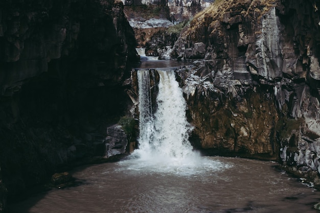 Beautiful shot of water flowing down into a pond in the middle of cliffs