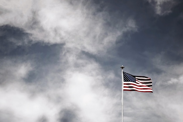 Free photo beautiful shot of the waving american flag on a white pole with amazing cloudy sky