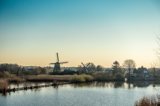 Free photo beautiful shot of the windmill near the river surrounded by trees and houses