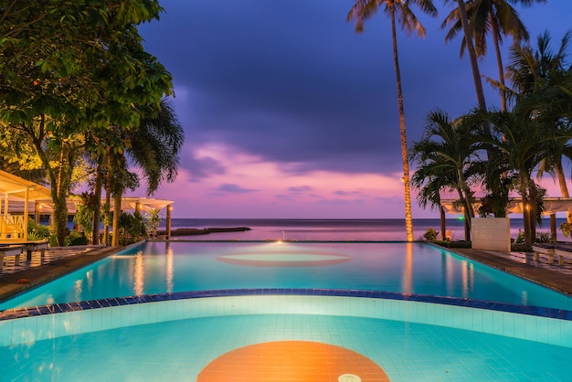 Free photo beautiful silhouette luxury umbrella and chair around swimming pool in hotel pool resort with coconut palm tree at sunrise times - boost up color processing