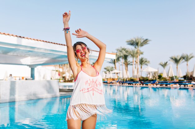 Beautiful slim girl in fringe shirt and white panties having fun near the warm blue water with palm trees on background