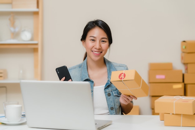 Beautiful smart Asian young entrepreneur business woman owner of SME checking product on stock scan qr code working at home. 