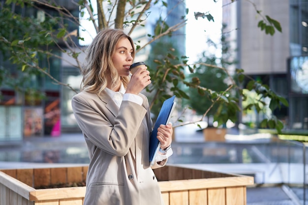 Free Photo beautiful smiling businesswoman drinks coffee on her working break standing on street