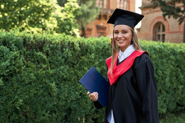 Beautiful smiling female graduate in graduation robe in university campus